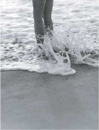 Bare feet stepping through pale sea foam at the shoreline