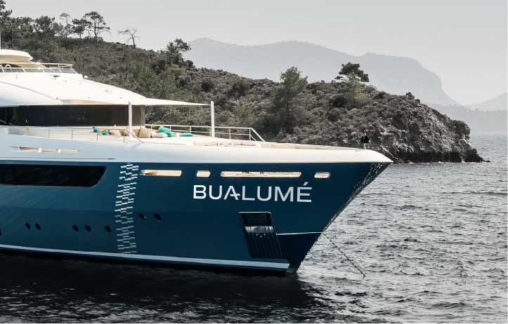 The bow of Bualume anchored near a quiet island shoreline